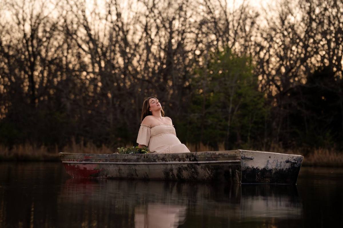 Expectant mother sitting in a weathered rowboat on still water at dusk