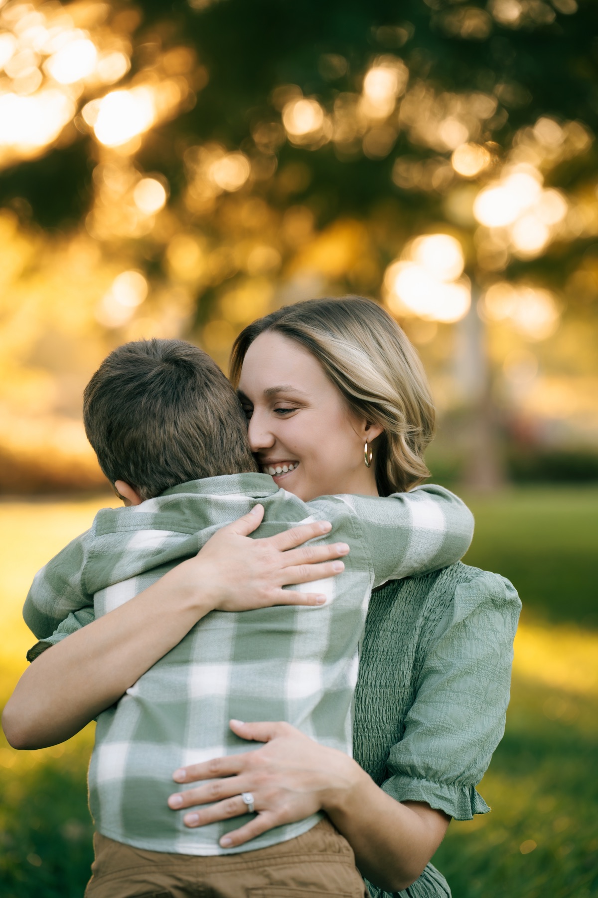 A woman hugging a child in a green plaid shirt outdoors.