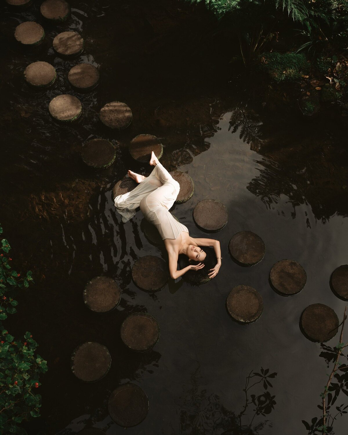 Woman in a white dress lying on stepping stones above dark water
