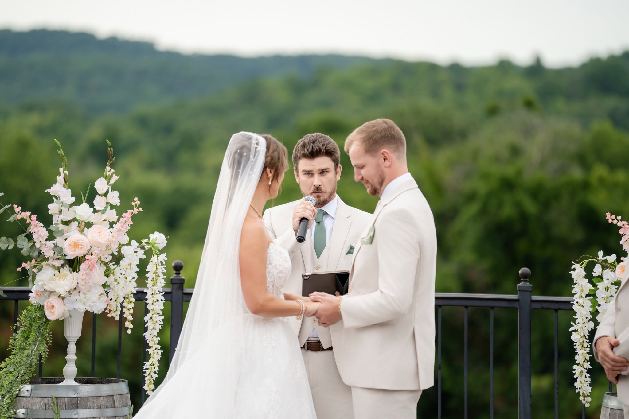 Couple exchanging vows with an officiant, flowers, and green hills behind them at Chandler Hill Vineyards