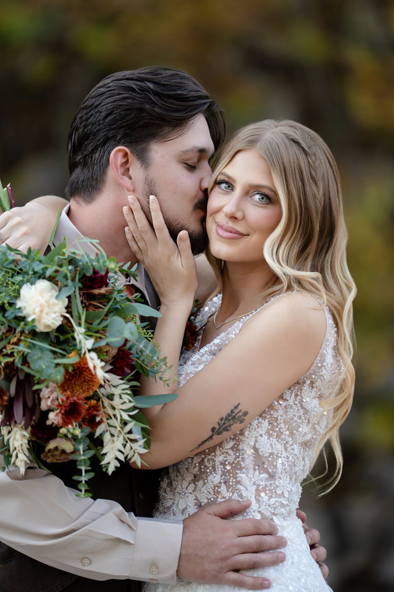 A couple embracing with a colorful bouquet as one kisses the other’s cheek