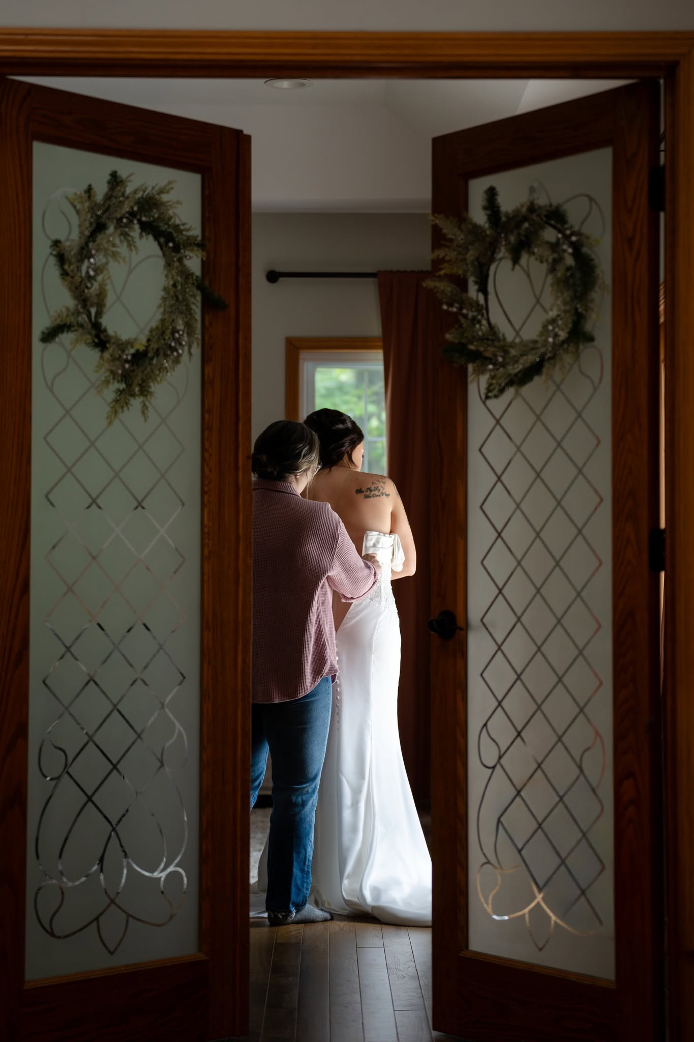 A bride having her dress fastened, photographed through open wooden doors
