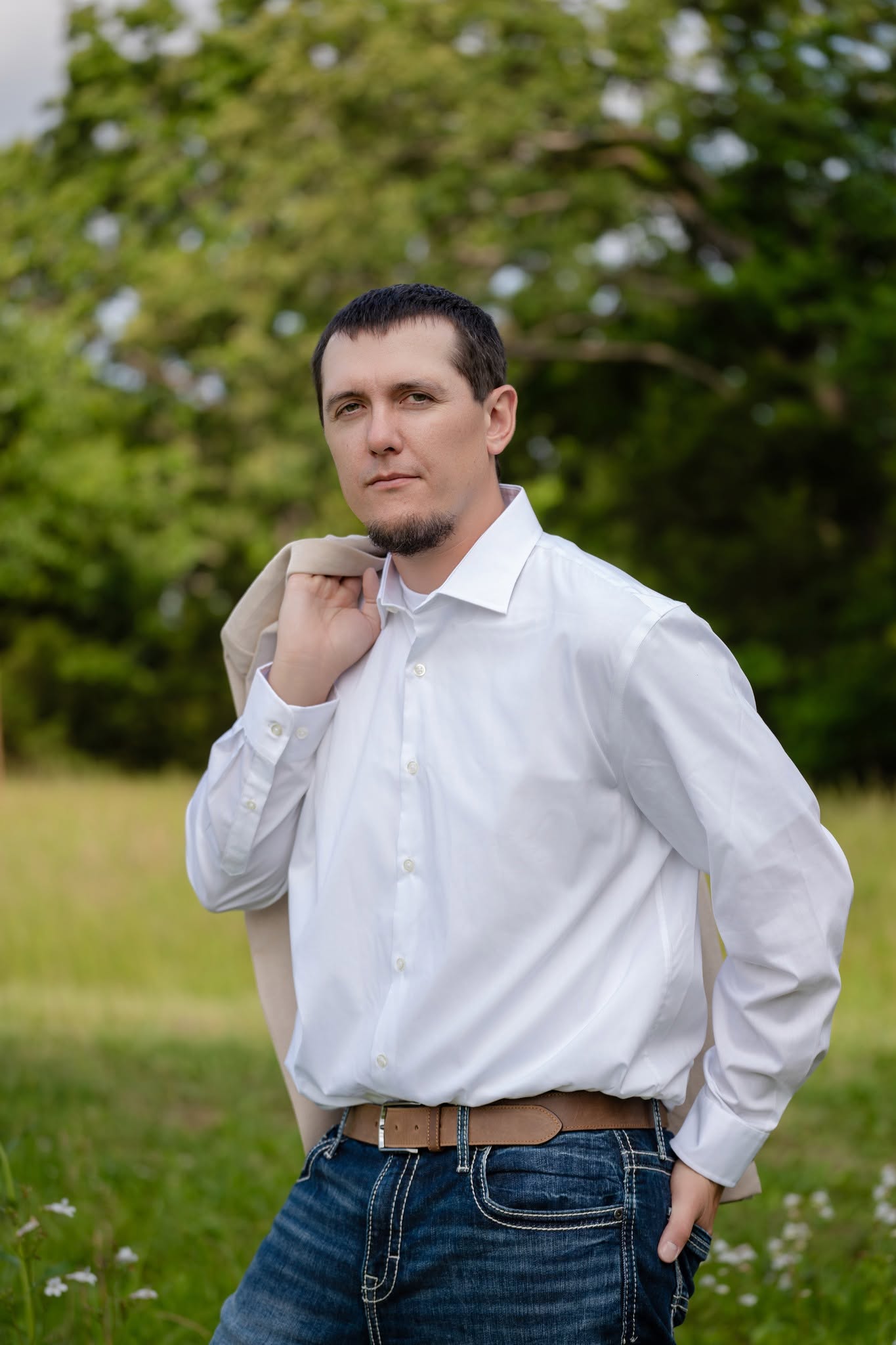 Groom in a white shirt carrying a tan jacket over his shoulder outdoors
