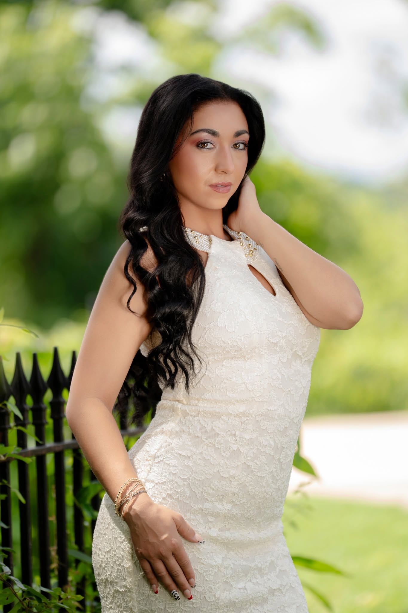 Portrait in a white lace dress beside a black fence and softly blurred greenery