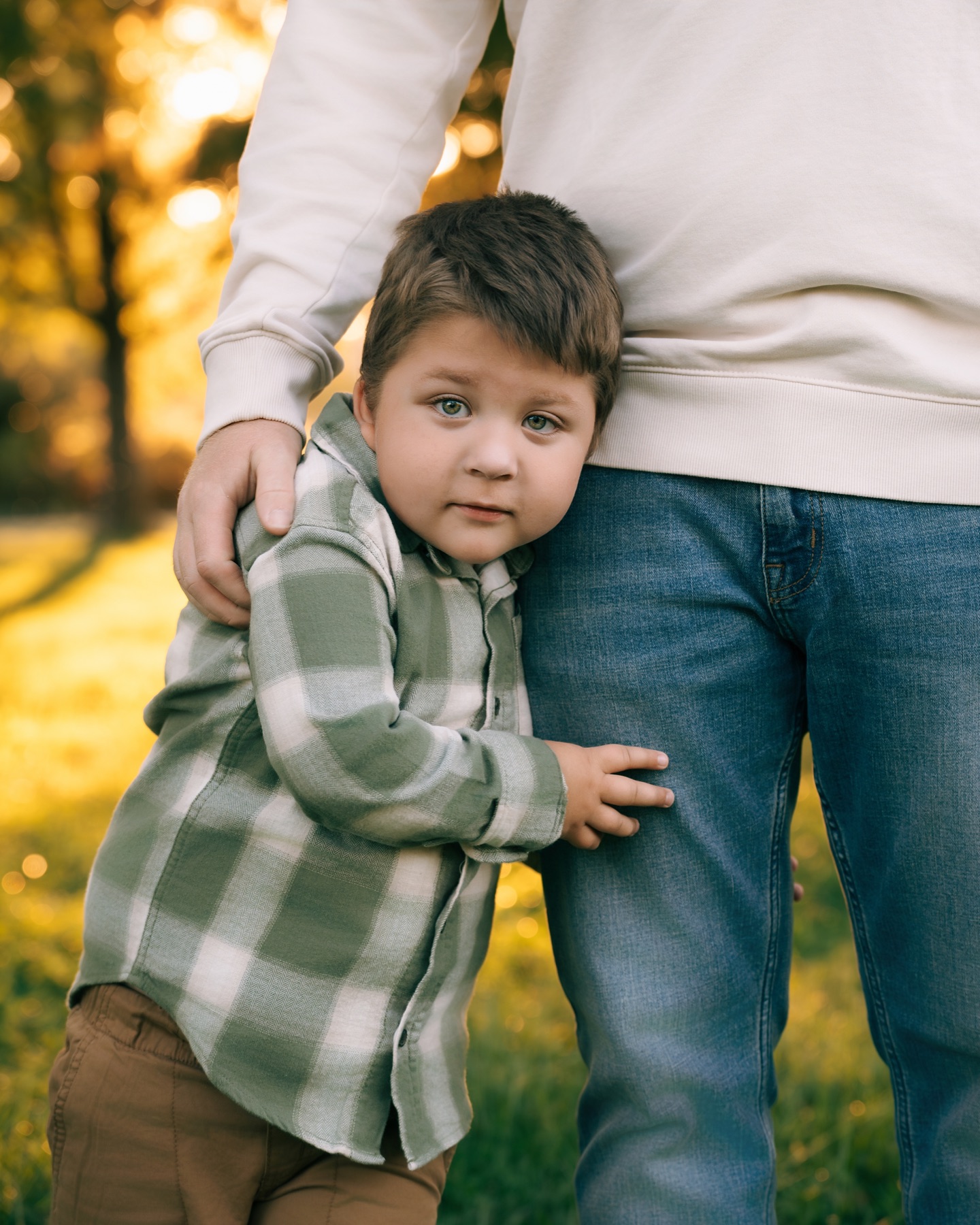 A child holding onto an adult’s leg during an outdoor family session.